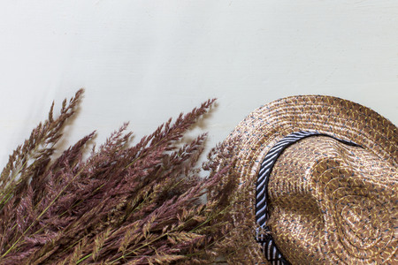 Straw hat and dru grass, reed on gray background with copy space.
