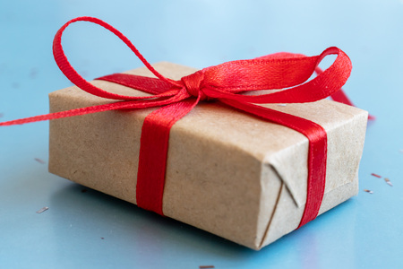 A gift box, beautifully wrapped with kraft paper and red ribbon and large bow on blue background.の写真素材