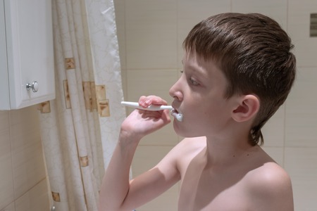 Boy brushing his teeth with a toothbrush in the bathroom.