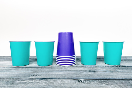 Four light blue empty and a stack of blue overturned take away disposable paper cups on wooden desk...