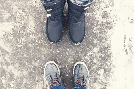 Two pair of legs wearing winter shoes stand opposite each other on snowy road.の写真素材
