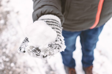 A boy wearing mittens, wool gloves holding a snowball in his hand, outdoor winter activities concept.の写真素材