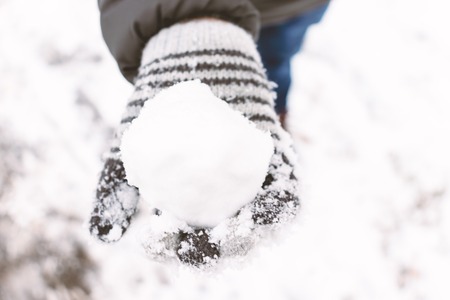 A boy wearing mittens, wool gloves holding a snowball in his hand, outdoor winter activities concept.の写真素材