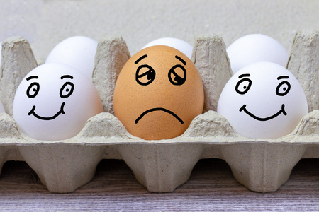 Brown egg with face expression of sad between two white happy eggs.