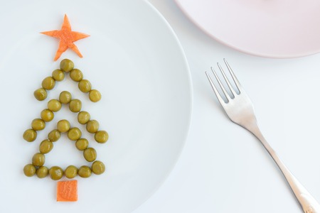 Fir tree made of peas and carrots on white plate on rustic white table background. New year and christmas concept, creative idea of celebratory meal.の写真素材