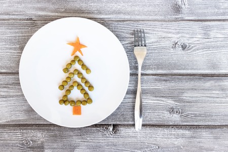 Fir tree made of peas and carrots on white plate on rustic wooden background. New year and christmas concept, creative idea of celebratory meal.の写真素材