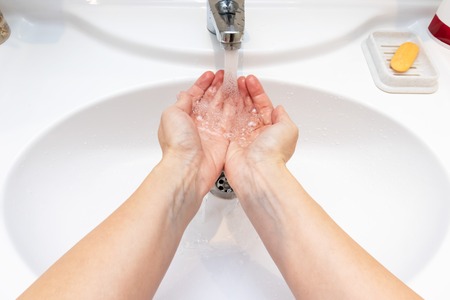 A woman wishing hands with water in bathroom sink. Desease prevention and hygiene concept. Useful, good habit.の写真素材