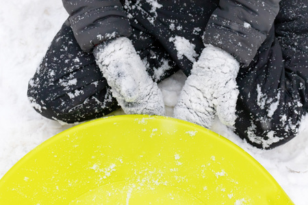 A boy of seven years old sitting on the snow and a green plastic saucer sled lying near him. Concept...