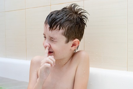 An eight year old boy sitting in bath with closed eyes and picking his nose.