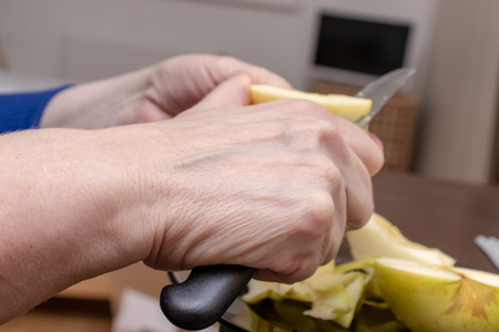 Female hands peeling skin off of a yellow apple with a knife.の写真素材