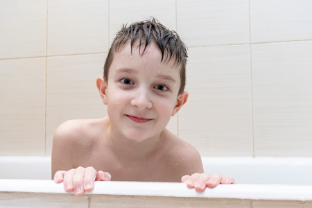 An eight year old boy sitting in bath and smiling.