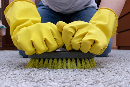 Cleaning carpet with a brush, hands in yellow rubber gloves doing home routine.