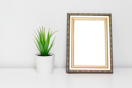 Minimalistic interior design with photo frame and a plant in white pot on a desk.