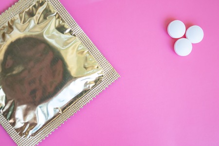 A condom in foil pack and three tablets on pink background with copy space.の写真素材
