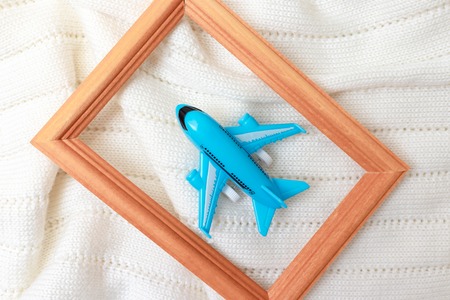 A blue toy plane in wooden frame on white knitted background, flat lay - trevelling and vacation...