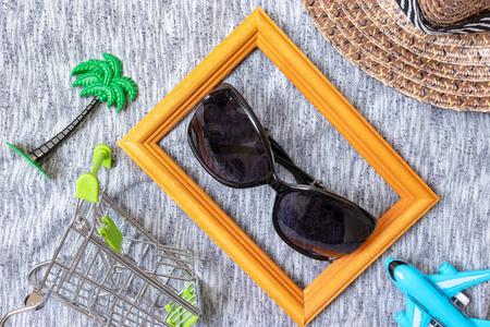 Shopping cart, straw hat, plane and sunglasses on textile background, flat lay - shopping tourism concept.の写真素材