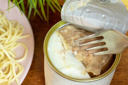 A tin, can of canned meat with a folk in it, italian pasta on a plate close up.