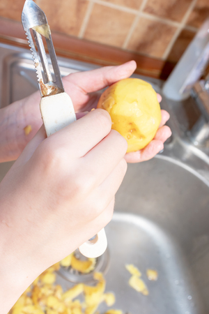 Hands of a teenager boy peeling potatoes with a peeling knife in the kitchen to help parents - children doing homework and cooking.の写真素材