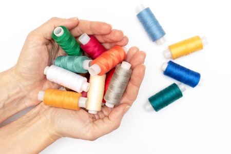 Hands holding a lot of colorful coils of thread close up, white background - hobby and DIY such as dressmaking ebroidery and needlework.の写真素材