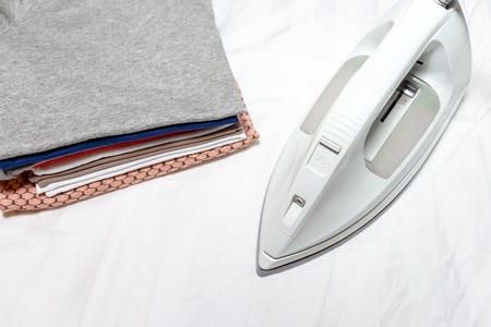 Modern electrical white iron near a stack of clothes close up - ironing, laundry and housework concept.の写真素材