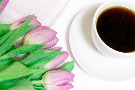 Bouquet of cut pink lilac tulips with a cup of coffee and notebook close up.の写真素材
