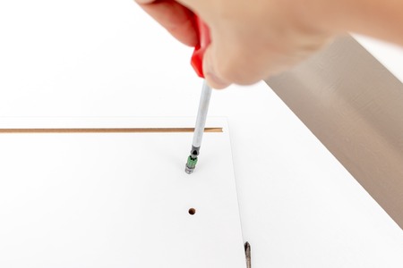 Assembling white furniture, she tighten a screw with a screwdriver, close up view.の写真素材