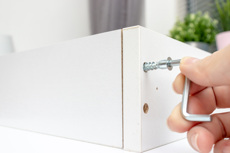 Close up view of a person assembling new white drawer using a screwdriver, tighten a screw with a hex allen key.の写真素材