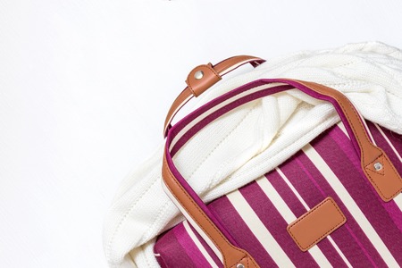 Red and white striped luggage bag with a knitted sweater on it , white background, minimal travel...