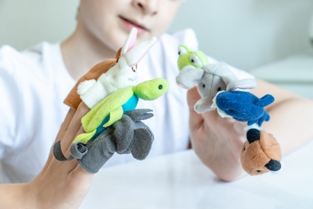 A caucasian boy playing different roles by using finger puppets, toys for expressing his emotions, agression, fear and freandship as a part of psychotherapy.の写真素材
