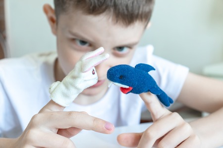 A caucasian boy playing different roles by using finger puppets, toys for expressing his emotions, agression, fear and freandship as a part of psychotherapy.の写真素材