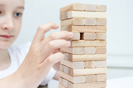 A preteen caucasian boy playing wooden block tower board game for practicing his physical and mental skill and entertainment.の写真素材