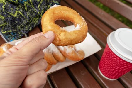 Family sitting on a bench in park and taking beignet pastries, donuts from a paper takeaway box and...