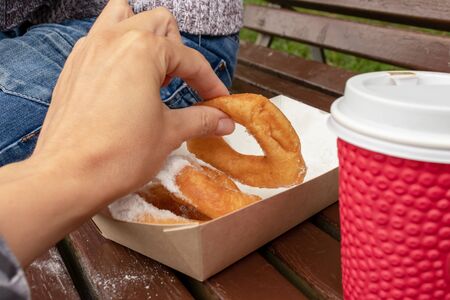 Family sitting on a bench in park and taking beignet pastries, donuts from a paper takeaway box and...