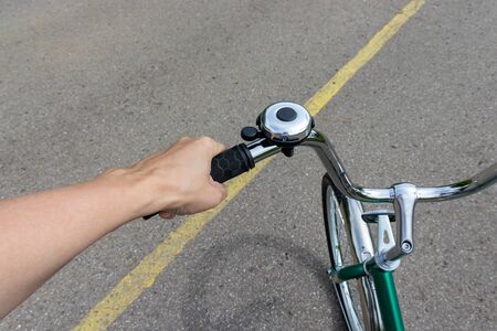 Female hand holding a bicycle handlebar and riding a bike on a road with yellow marking, bicycle...