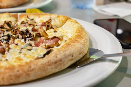 Italian fast food, delicious hot pizza with bacon and mushrooms sliced and served on a white plate, close.の写真素材