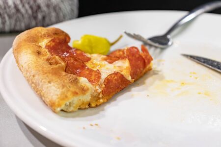 A slice of pepperoni pizza on white plate with folk and knife on a table of italian restaurant.の写真素材
