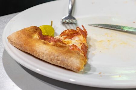 A slice of pepperoni pizza on white plate with folk and knife on a table of italian restaurant.の写真素材
