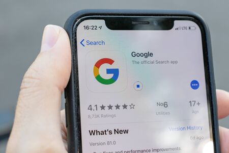 MOSCOW, RUSSIA - SEPTEMBER 01, 2019: Hand holding a smartphone with google application icon on screen. Google app icon in play market, city park on background.のeditorial素材