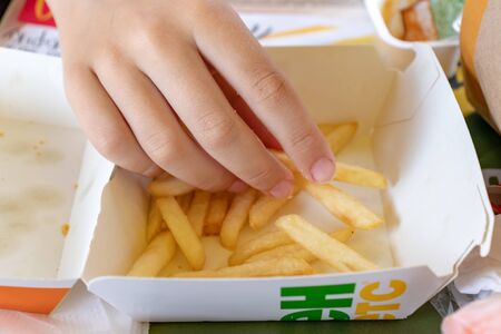 Moscow, Russia - July 26, 2019: A teenager hand taking a piece of french fries out of a paper disposable takeaway box in Macdonalds fast food restaurantのeditorial素材