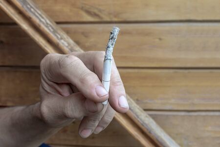 Man holding a lighted cigarette in fingers with a lot of ashes, bad habbits and nicotine addiction concept.の写真素材