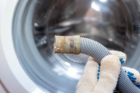 Hand of a plumber holding a broken flexible drain hose of washing machine, clogged and covered with lime scale, dirt limescale and rust.の写真素材