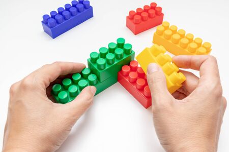 Hands constructing from colorful toy plastic bricks, blocks for building on white background.