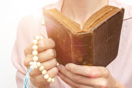 Young praying christian woman's hands with a rosary and holy bible .