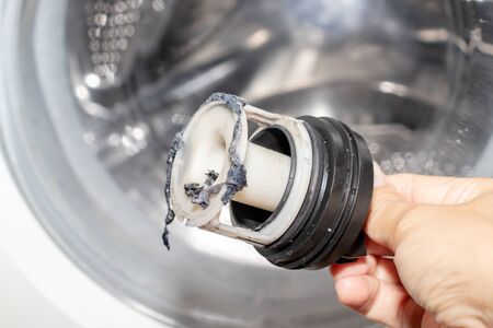Inspecting washing machine's dirty clogged drain pump filter close up, clean and repair.