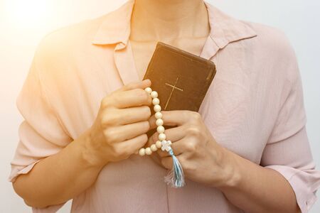 Young praying christian woman's hands with a rosary and holy bible .