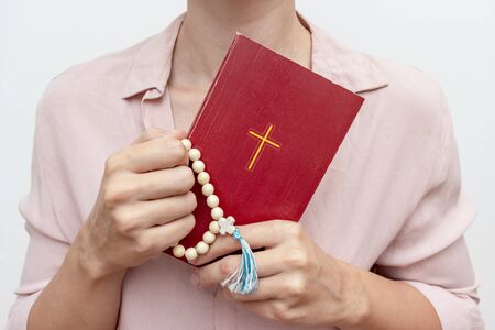Young praying christian woman's hands with a rosary and holy bible .