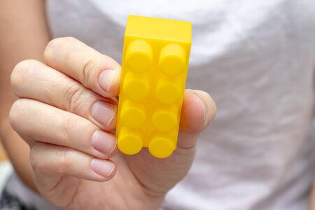 Woman holding colorful yellow toy plastic bricks, blocks for building, playing games and...