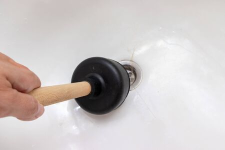 Woman hand holding a plunger to clean bathtub drain, sewer clogged, blocked with fallen out hair.の写真素材