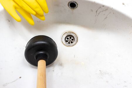 Blocked sewer, clogged wash bowl, basin drain, yellow rubber gloves and a plunger near in the bathroom at home.の写真素材