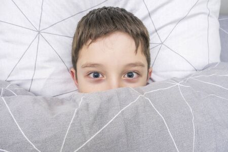 Top view of a scared boy in bed covering his face with blanketの写真素材